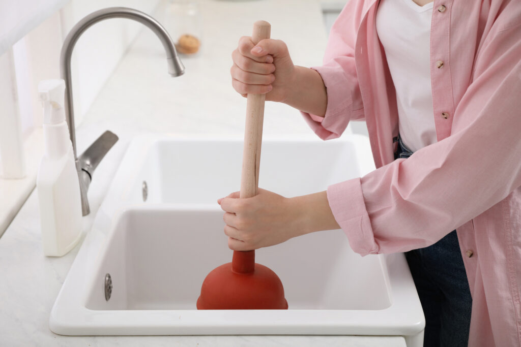 person using plunger to unclog sink